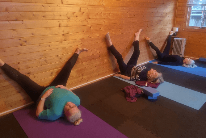Yoga Class in Croxley Green Women in a Croxley Green yoga class lying on mats with legs supported against a wooden wall during a gentle stretch.